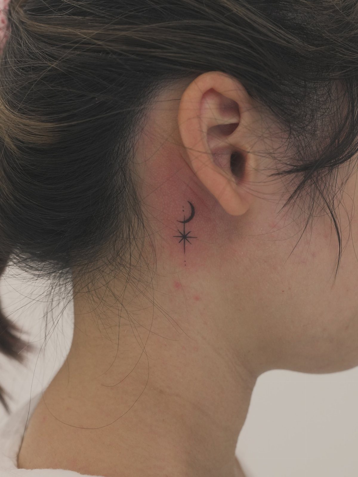Fine Line Tattoo Placement: 11 Ideas That Actually Work 7 A small crescent moon and star fine line tattoo located behind a person's ear.