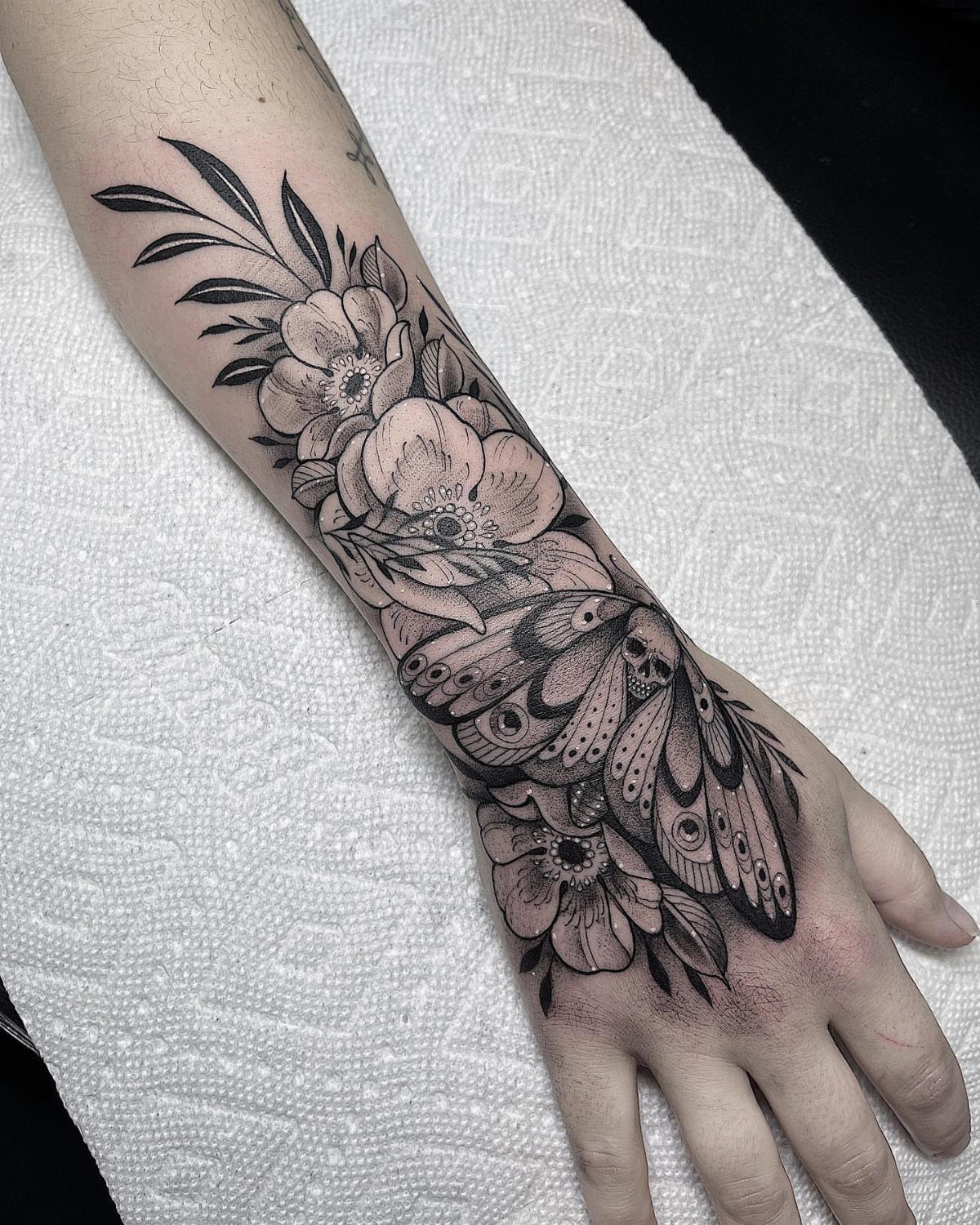 Tattoo Style for Hand: 8 Designs That Work on This Spot 2 Black and grey floral and moth tattoo covering a person's forearm and hand.
