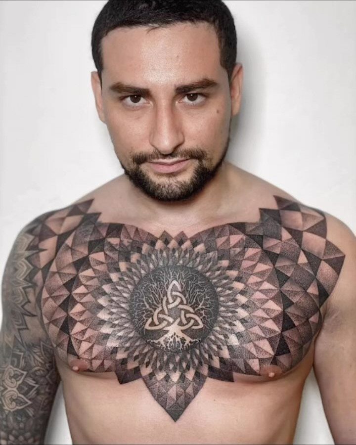 Tattoo at Chest: 15 Ideas from Wing Spread to Underboob 2 A man displaying a large, symmetrical geometric and mandala style tattoo across his chest.