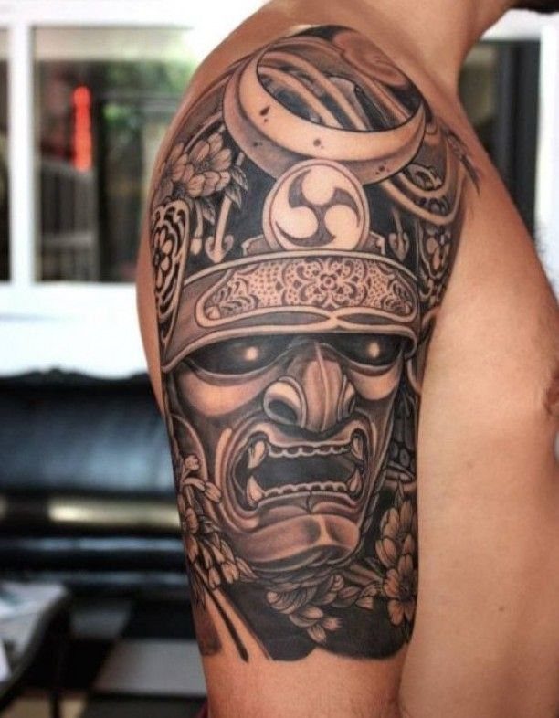 Japanese Tattoo Style: 14 Iconic Motifs and Where They Go 5 A detailed black and grey samurai helmet tattoo covering a person's shoulder and upper arm.