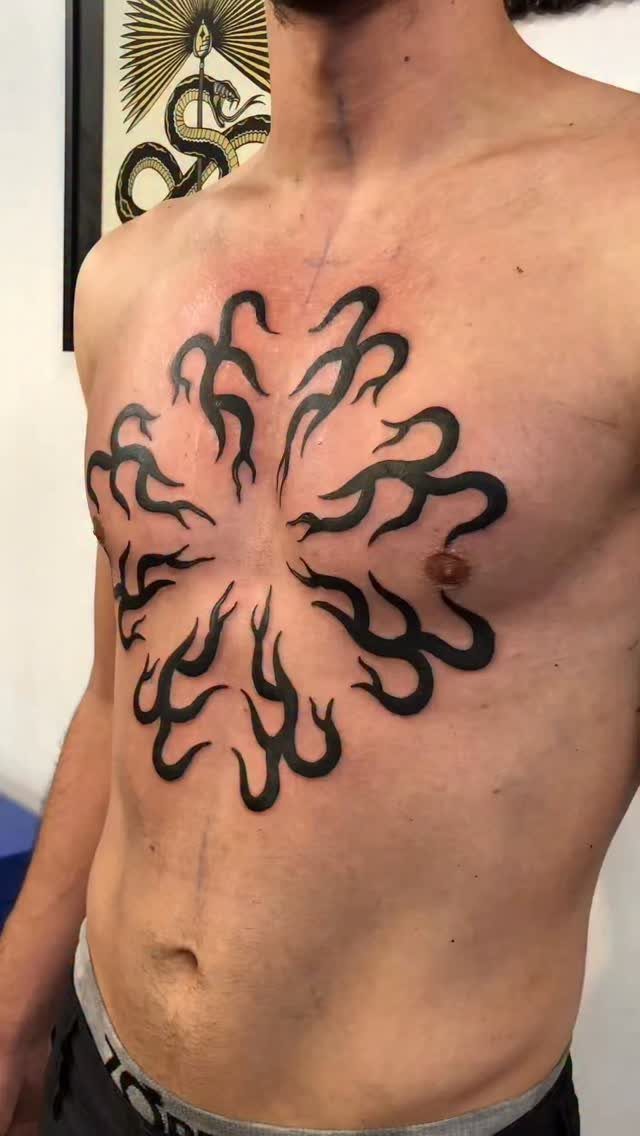Tattoo at Chest: 15 Ideas from Wing Spread to Underboob 11 A man with a large black tribal tattoo on his chest featuring swirling flame-like patterns.