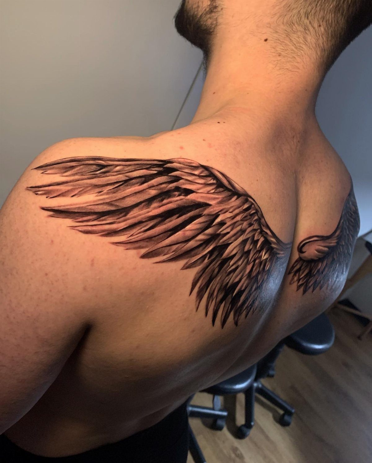 12 Back Tattoo Goth Styles for Spine, Skulls, and Full Backpieces 7 Large black ink feathered angel wings tattooed across a man's upper back and shoulders.