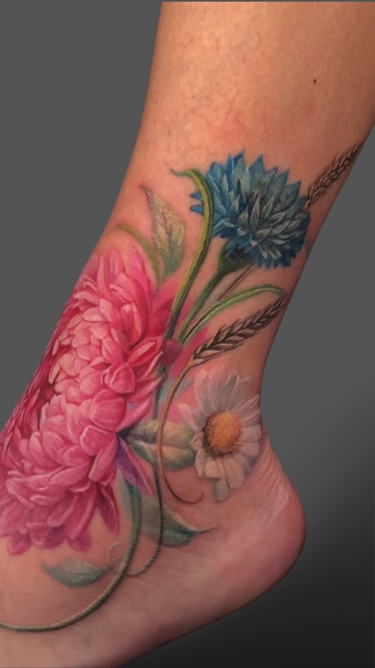 14 Places for a Tattoo for Women: From Ankle to Neck 6 A colorful floral tattoo with pink, blue, and white flowers on a person's ankle.