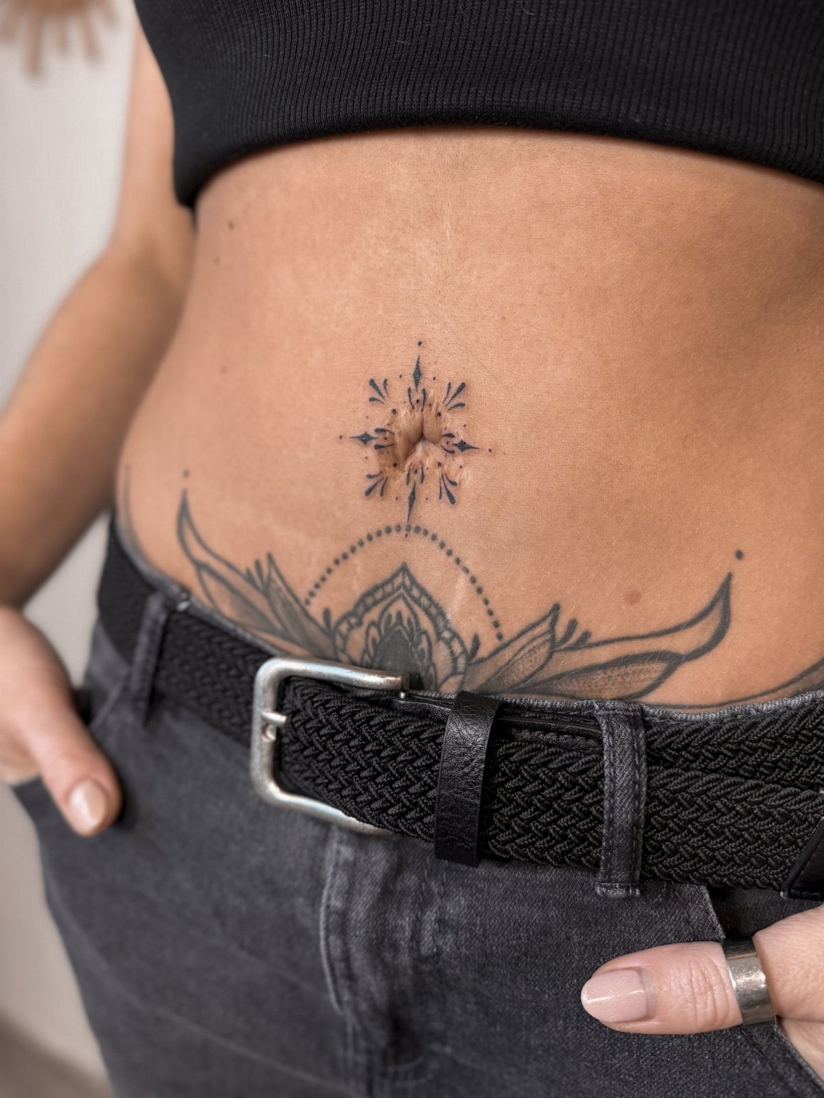 A small starburst tattoo design centered around a person's belly button on their abdomen.