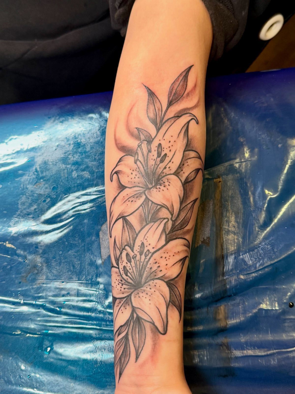 High Contrast Tattoo Design: 8 Bold Ideas That Read From Any Distance 5 Black ink lily flower tattoo with detailed shading on a person's forearm.