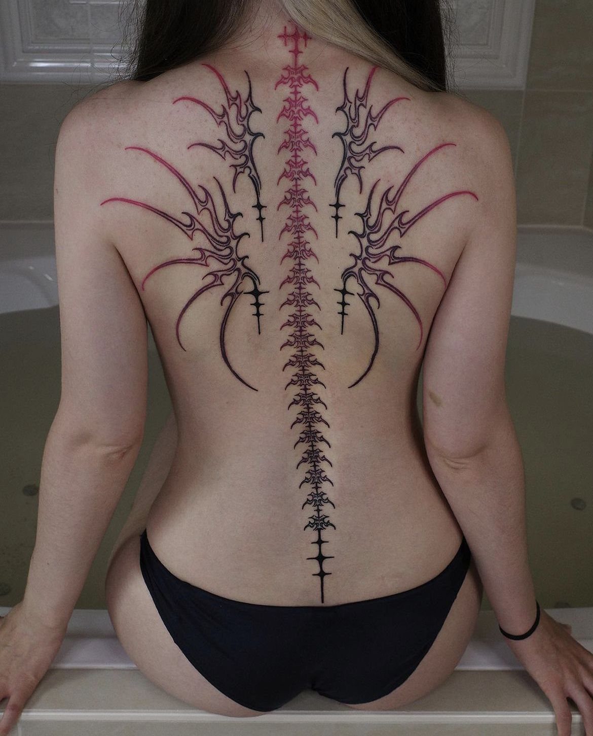 12 Back Tattoo Goth Styles for Spine, Skulls, and Full Backpieces 13 A person's back displaying a large, symmetrical black and red neotribal spine tattoo.