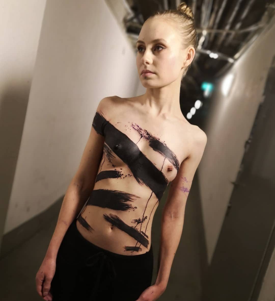 Tattoo Pattern Abstract: 10 Design Ideas for Your Next Ink 8 A young woman with large black abstract brushstroke tattoos across her torso standing in a hallway.
