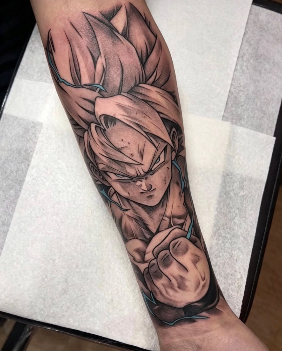 9 Tattoo Style Anime Ideas for Your First Ink or Next Sleeve 8 Black and grey anime character tattoo on a person's forearm with blue accents.