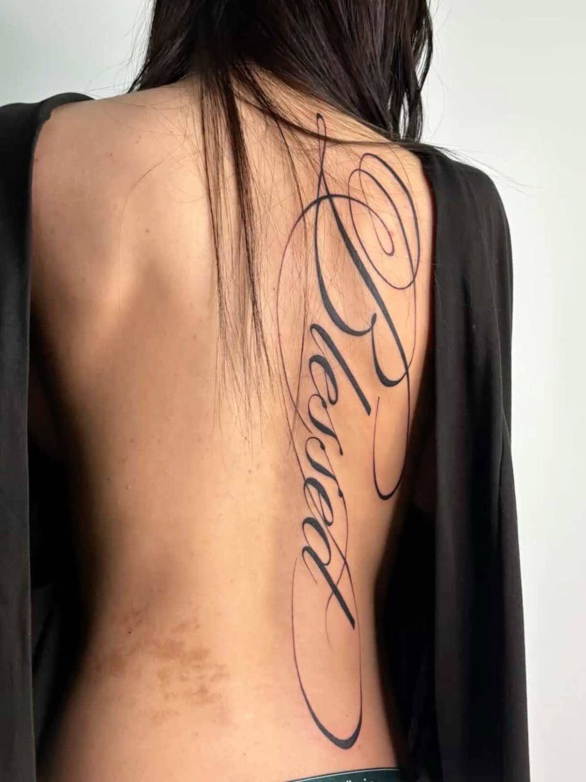 11 Lower Back Script Tattoos for Bold Ink Inspiration 3 A vertical black ink script tattoo of the word Blessed on a person's back.