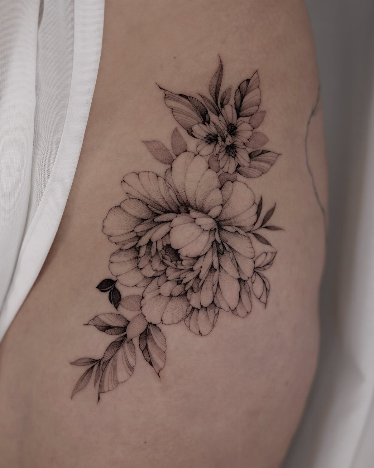 A black ink tattoo of large blooming peonies with detailed petals on human skin.