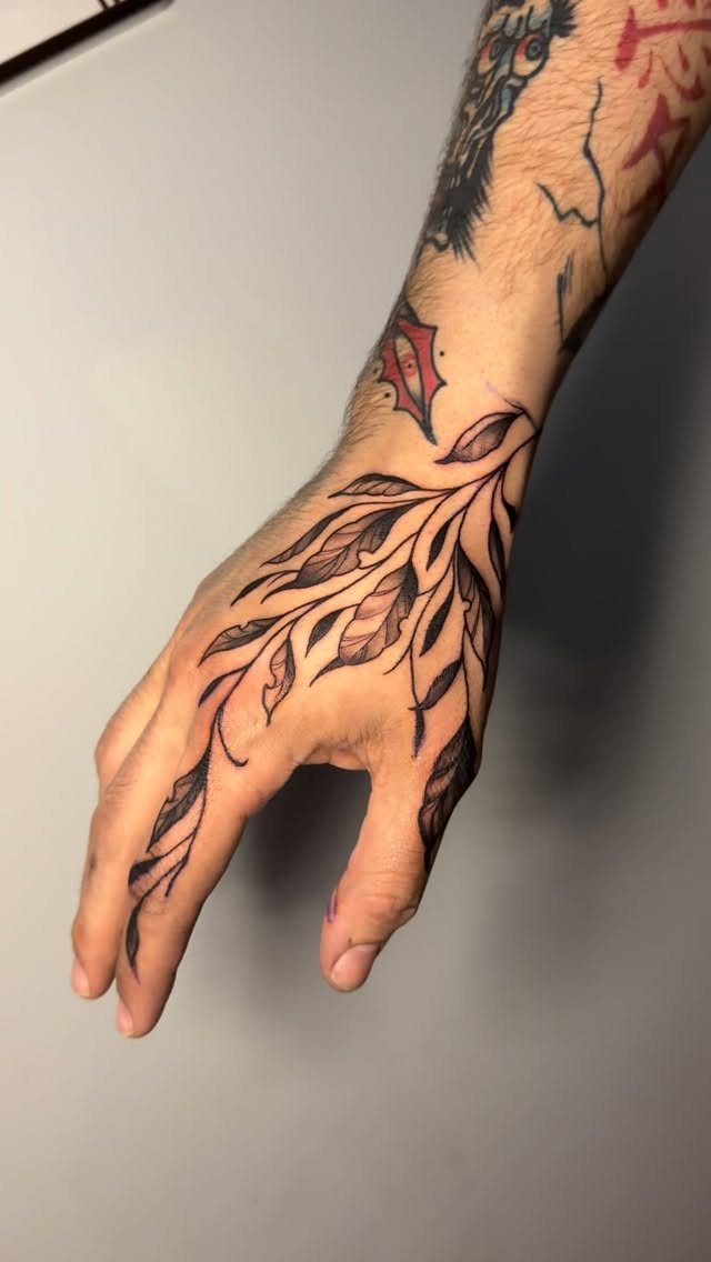 Botanical Tattoo Blackwork: 8 Ideas for Ink That Grows on Skin 6 A hand with a black ink botanical tattoo featuring flowing leaves and stems.