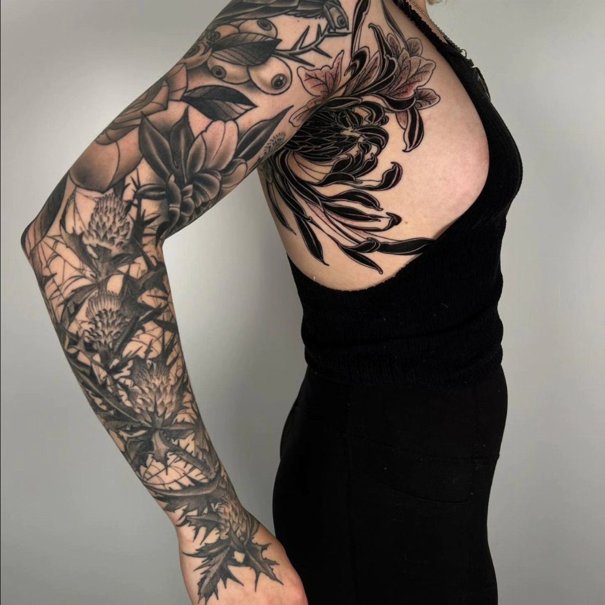 A person's arm and shoulder covered in a detailed blackwork botanical tattoo.