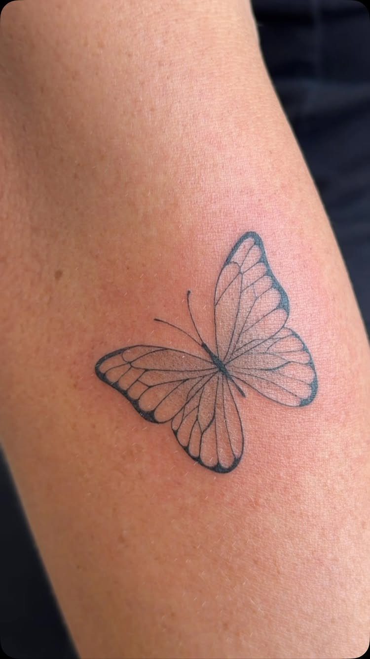 A black ink butterfly tattoo with fine lines on a person's skin.