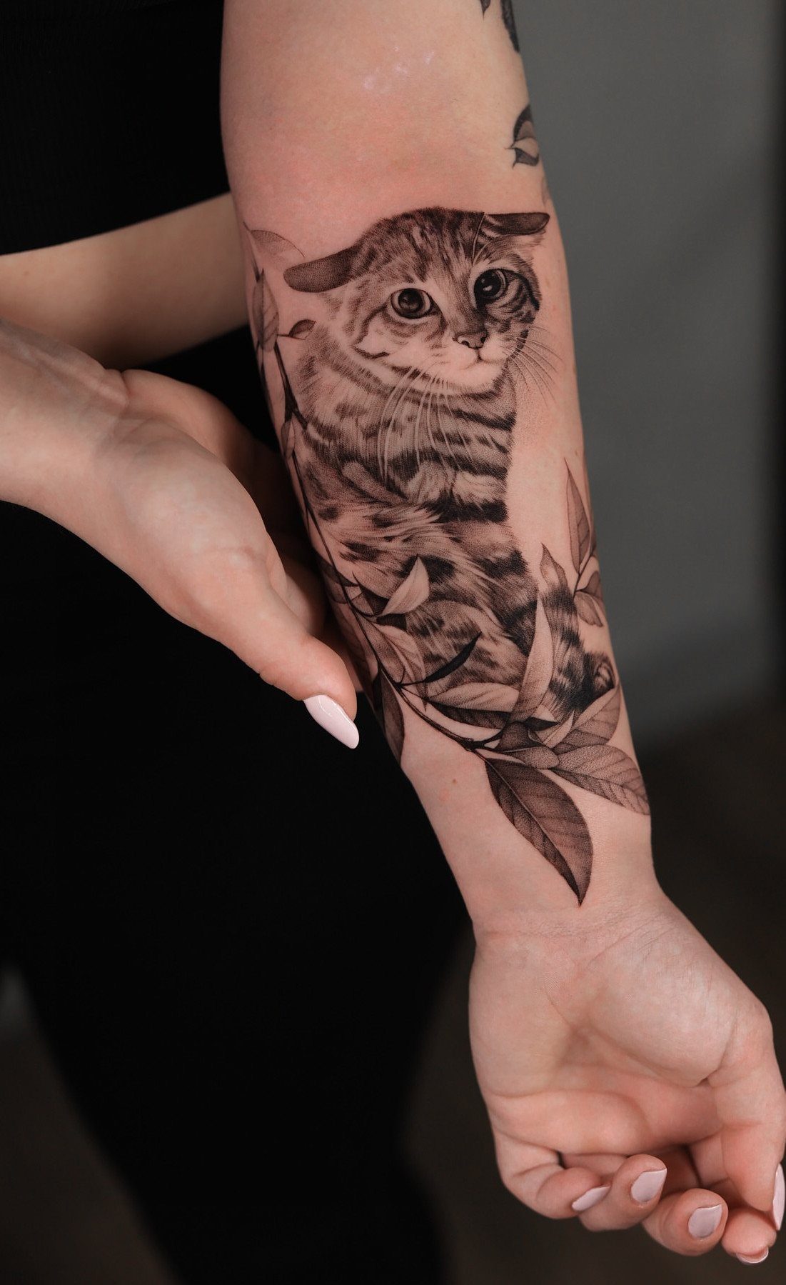 High Contrast Tattoo Design: 8 Bold Ideas That Read From Any Distance 8 A detailed black and grey cat tattoo with leaves on a person's forearm.