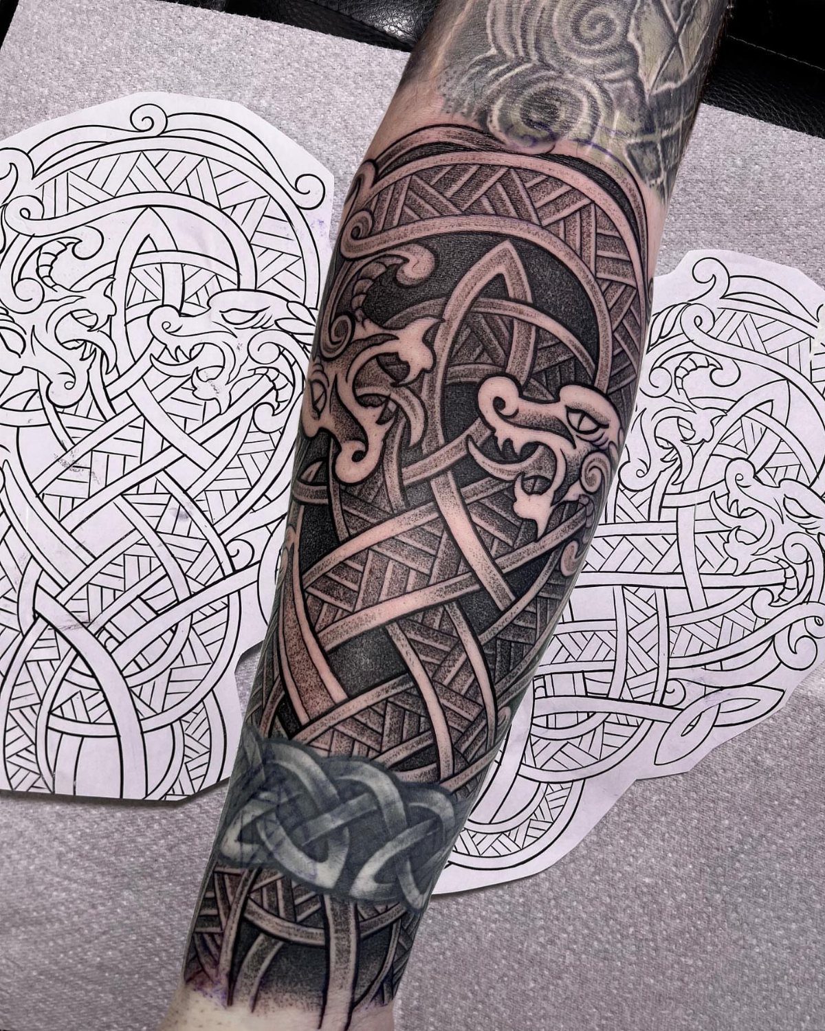 Celtic Pagan Tattoo: 6 Design Ideas and Flash Art 2 A detailed black and grey Celtic knotwork tattoo with animal motifs on a person's forearm.
