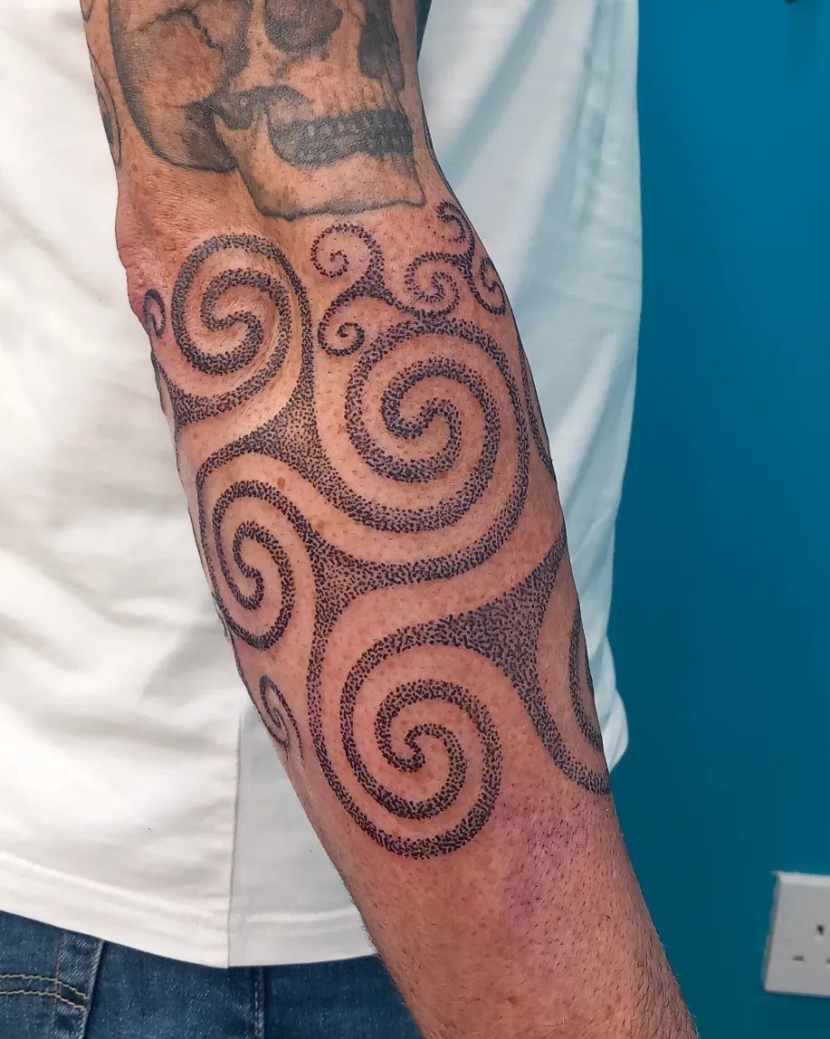 Celtic Pagan Tattoo: 6 Design Ideas and Flash Art 3 A forearm featuring a large black dotwork Celtic triskele spiral tattoo design.