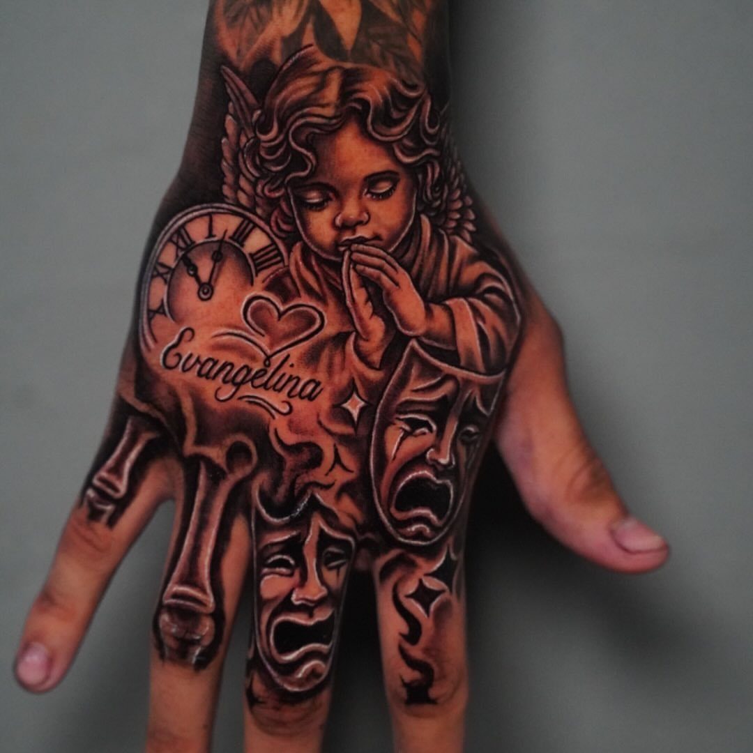 Tattoo Style for Hand: 8 Designs That Work on This Spot 9 A detailed black and grey hand tattoo featuring a cherub, a clock, and theatrical masks.