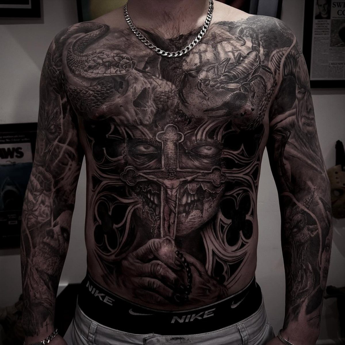 Man with large black and grey tattoos covering his entire chest and stomach area.