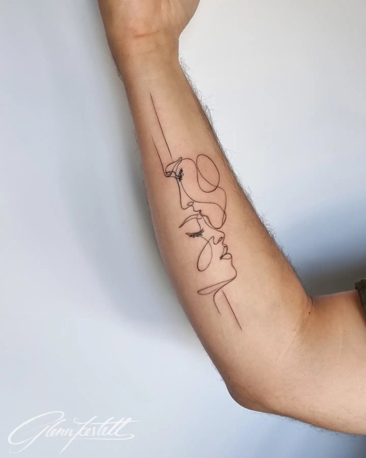A continuous line drawing tattoo of two faces on a person's forearm.