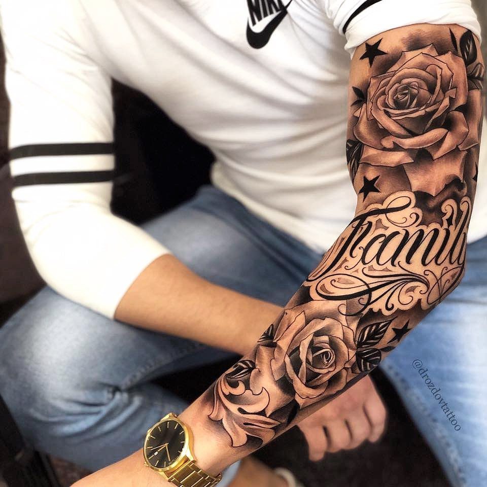 A person's arm featuring a large black and grey tattoo of blooming roses and script text.