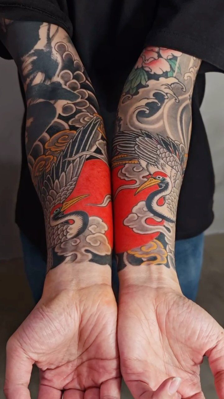 Japanese Tattoo Style: 14 Iconic Motifs and Where They Go 13 Two forearms displaying detailed Japanese style tattoos of cranes, waves, and cherry blossoms.