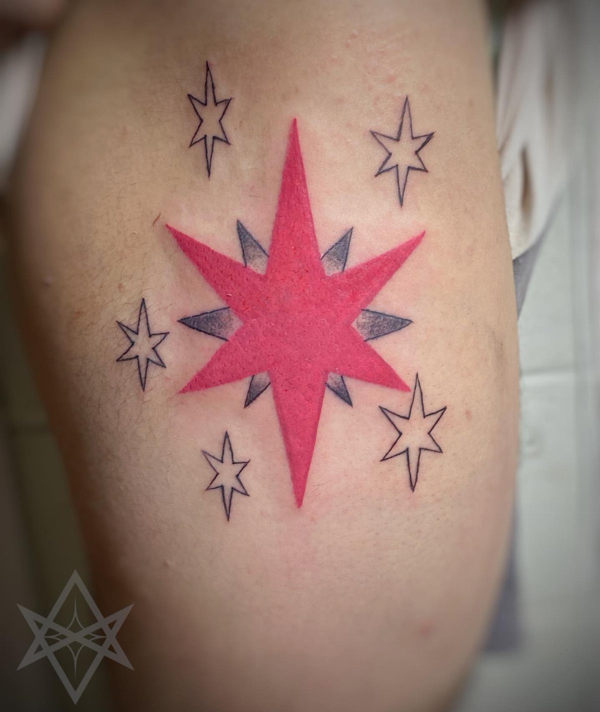 A pink and black star tattoo on a person's skin surrounded by smaller stars.