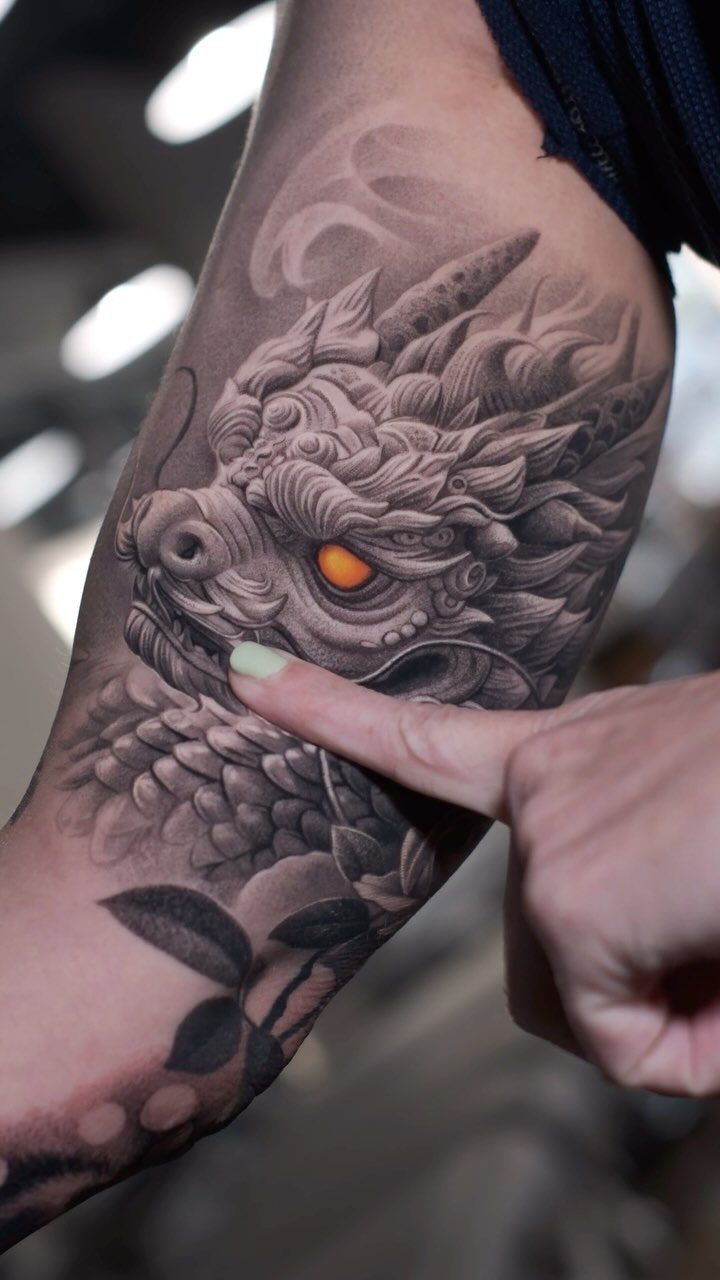 11 Tattoo Arm Women Will Want to See Before Booking 2026 9 A detailed black and grey dragon tattoo with an orange eye on a woman's arm.
