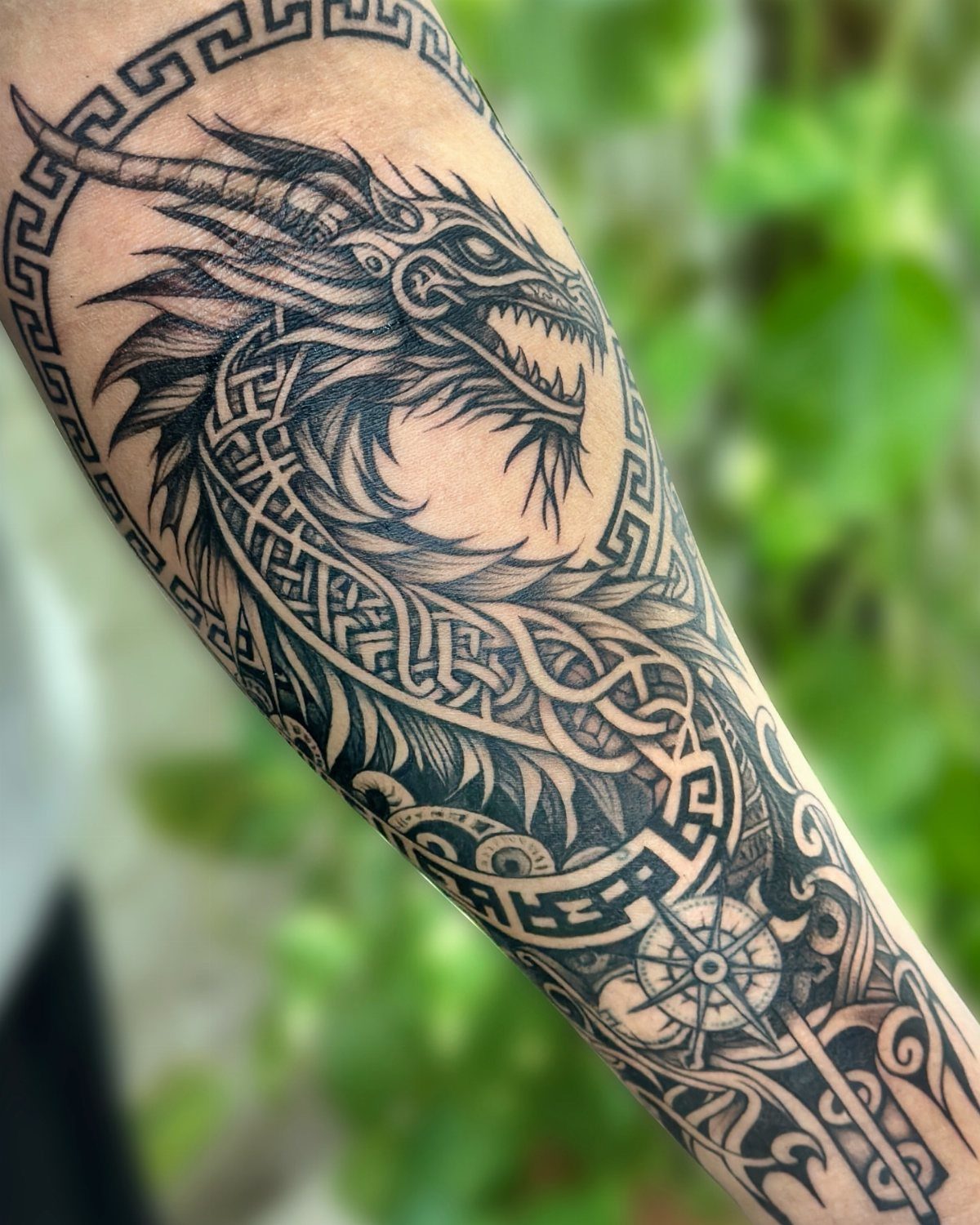 A detailed black ink dragon tattoo with tribal patterns on a person's arm.