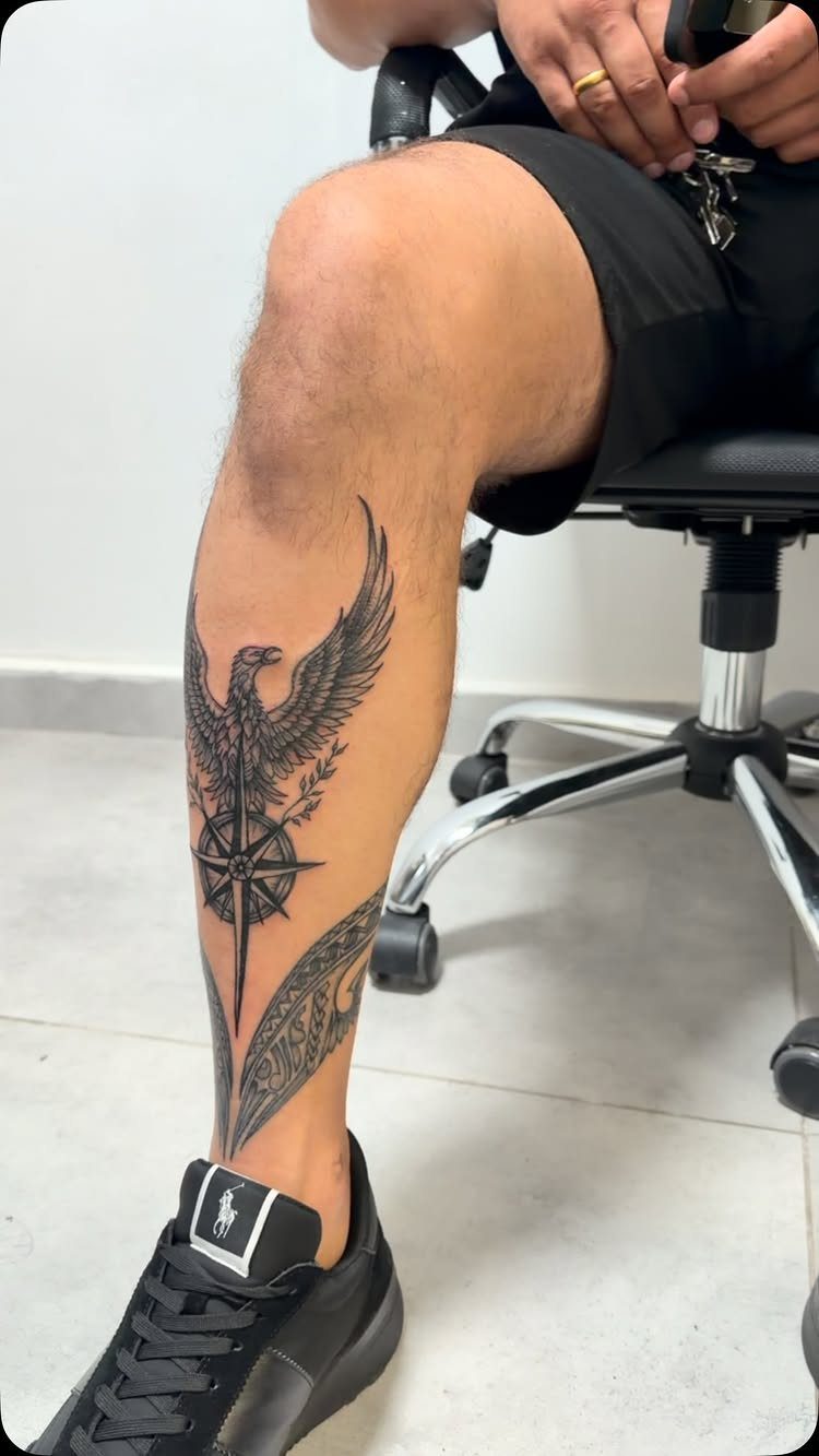 16 Front Ankle Tattoo Ideas for Women 2026 15 A large black ink eagle and compass tattoo on a person's lower leg and ankle.