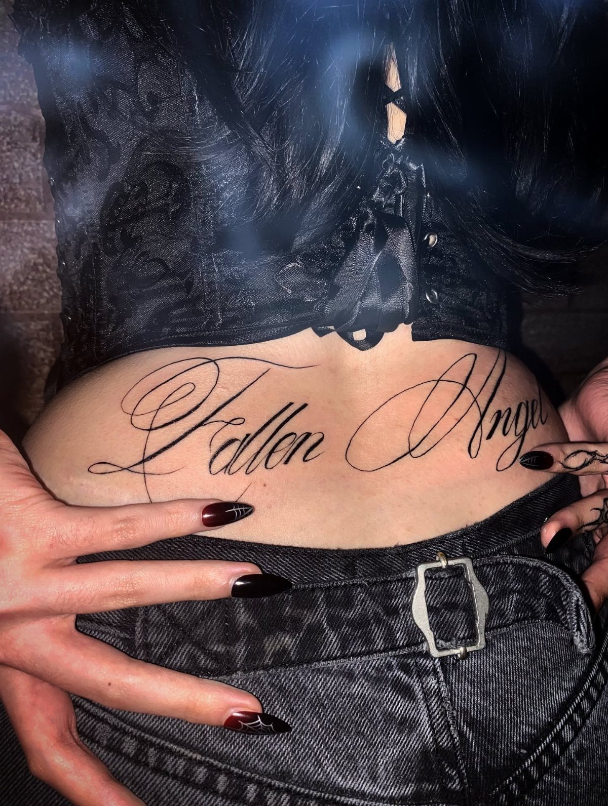 11 Lower Back Script Tattoos for Bold Ink Inspiration 11 A lower back tattoo in large cursive script reading Fallen Angel on a person.