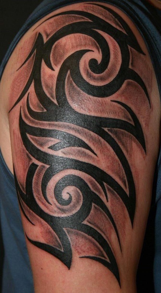 A large black tribal tattoo with sharp, curved patterns on a person's upper arm.