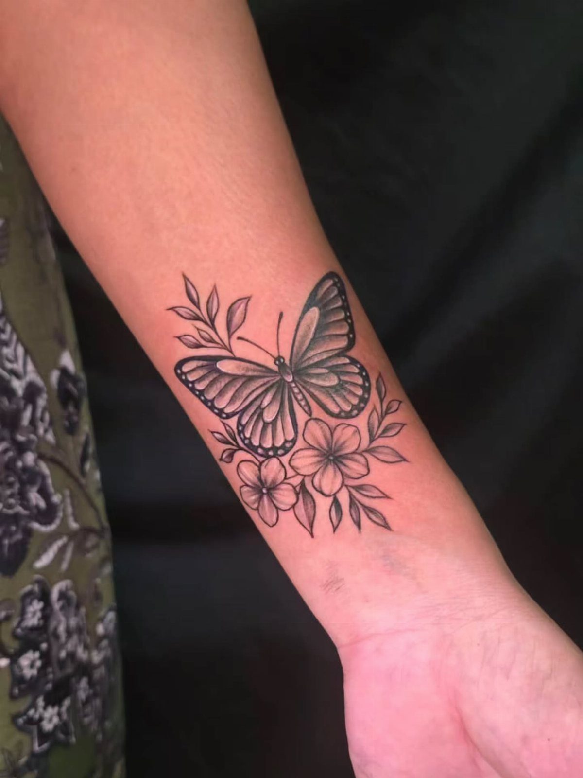 A black ink tattoo of a butterfly and flowers on a person's forearm.