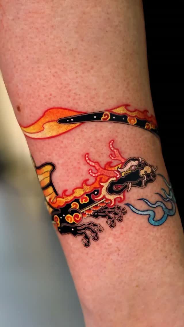 Tattoo Pattern Dragon: 11 Ideas for Ink That Follows the Body 9 A colorful dragon tattoo with orange flames and blue smoke on a person's forearm.