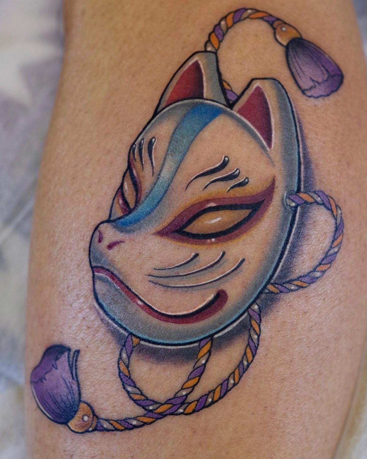 Japanese Tattoo Style: 14 Iconic Motifs and Where They Go 11 A colorful Japanese fox mask tattoo with blue and red accents on human skin.