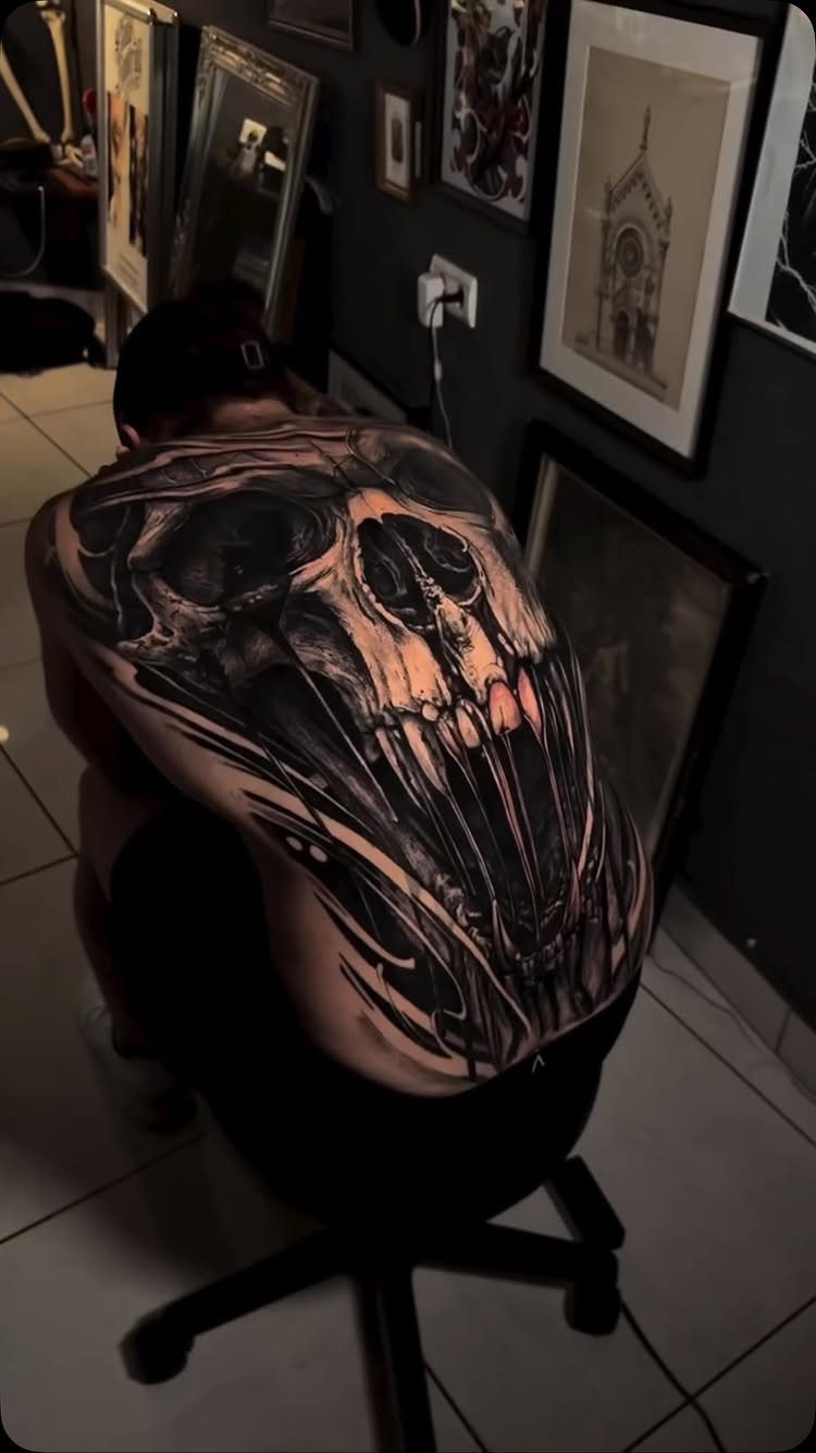 12 Back Tattoo Goth Styles for Spine, Skulls, and Full Backpieces 11 A large black ink skull tattoo covering a person's entire back in a dark room.