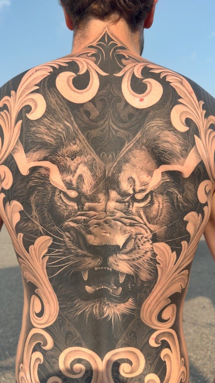 Tattoo Placement on Back: 6 Areas for Your Next Ink 4 A man's back featuring a large, intricate lion tattoo surrounded by decorative swirling patterns.