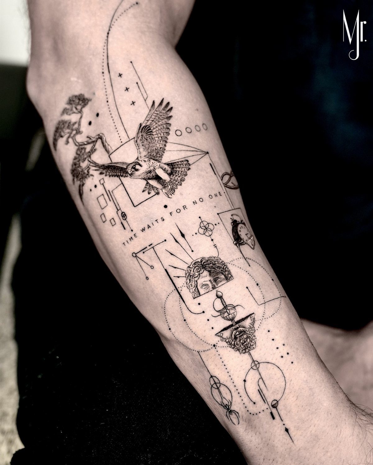 A detailed black ink forearm tattoo featuring a bird, a face, and geometric line work.