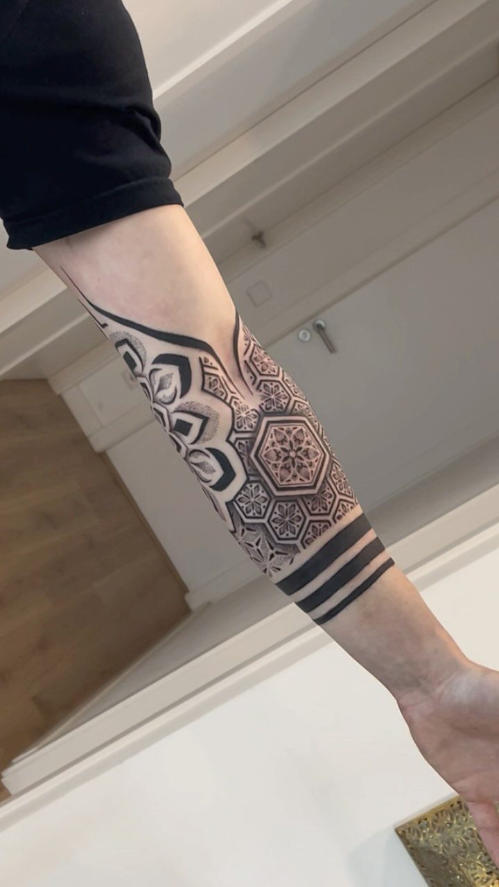 17 Tattoo Pattern on Arm Ideas: From Fine Line to Full Sleeve 8 A forearm displaying a large black ink tattoo with intricate geometric patterns and mandala designs.