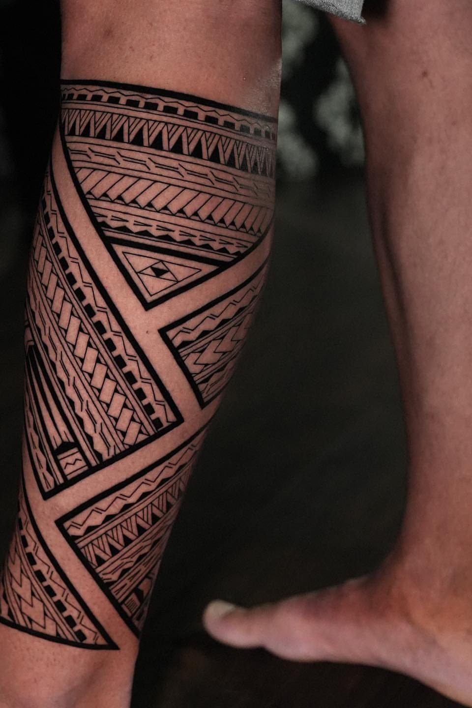 A person's leg featuring a large black geometric tribal tattoo wrapping around the calf.