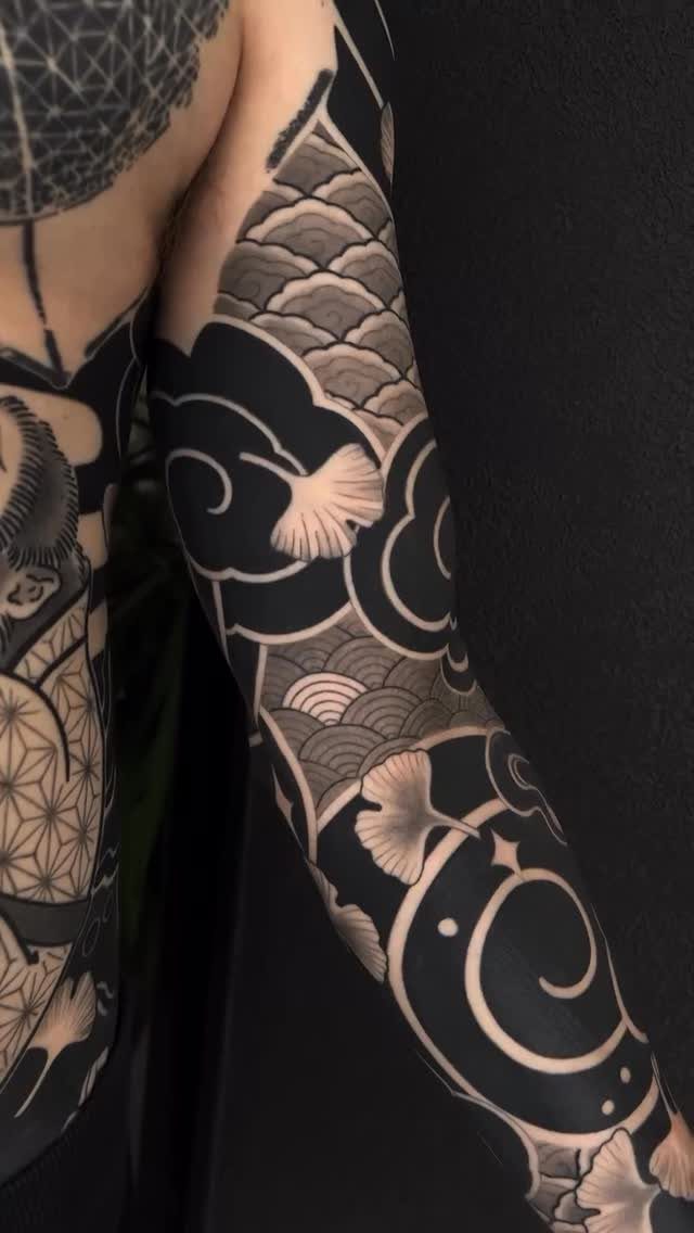 17 Tattoo Pattern on Arm Ideas: From Fine Line to Full Sleeve 15 A person's arm featuring a large black and grey sleeve tattoo with swirling patterns and leaves.