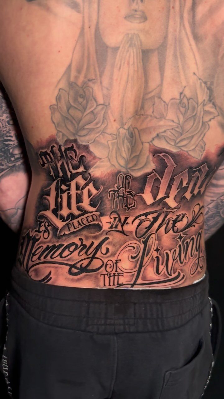 11 Lower Back Script Tattoos for Bold Ink Inspiration 7 A large black and red gothic script tattoo on a person's lower back.
