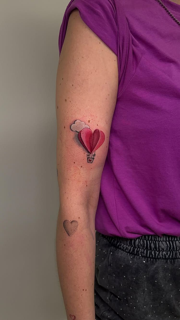 A small pink heart-shaped hot air balloon tattoo on a person's arm.