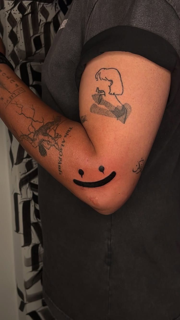 17 Tattoo Pattern on Arm Ideas: From Fine Line to Full Sleeve 4 A person's arm displaying small, minimalist black ink tattoos including a profile and a smiley face.