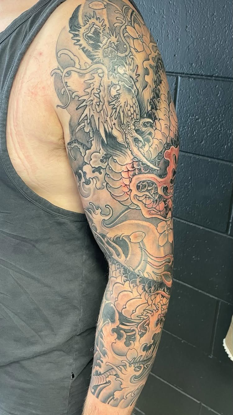 Japanese Tattoo Style: 14 Iconic Motifs and Where They Go 2 A detailed Japanese dragon tattoo covering a person's entire arm with black and red ink.