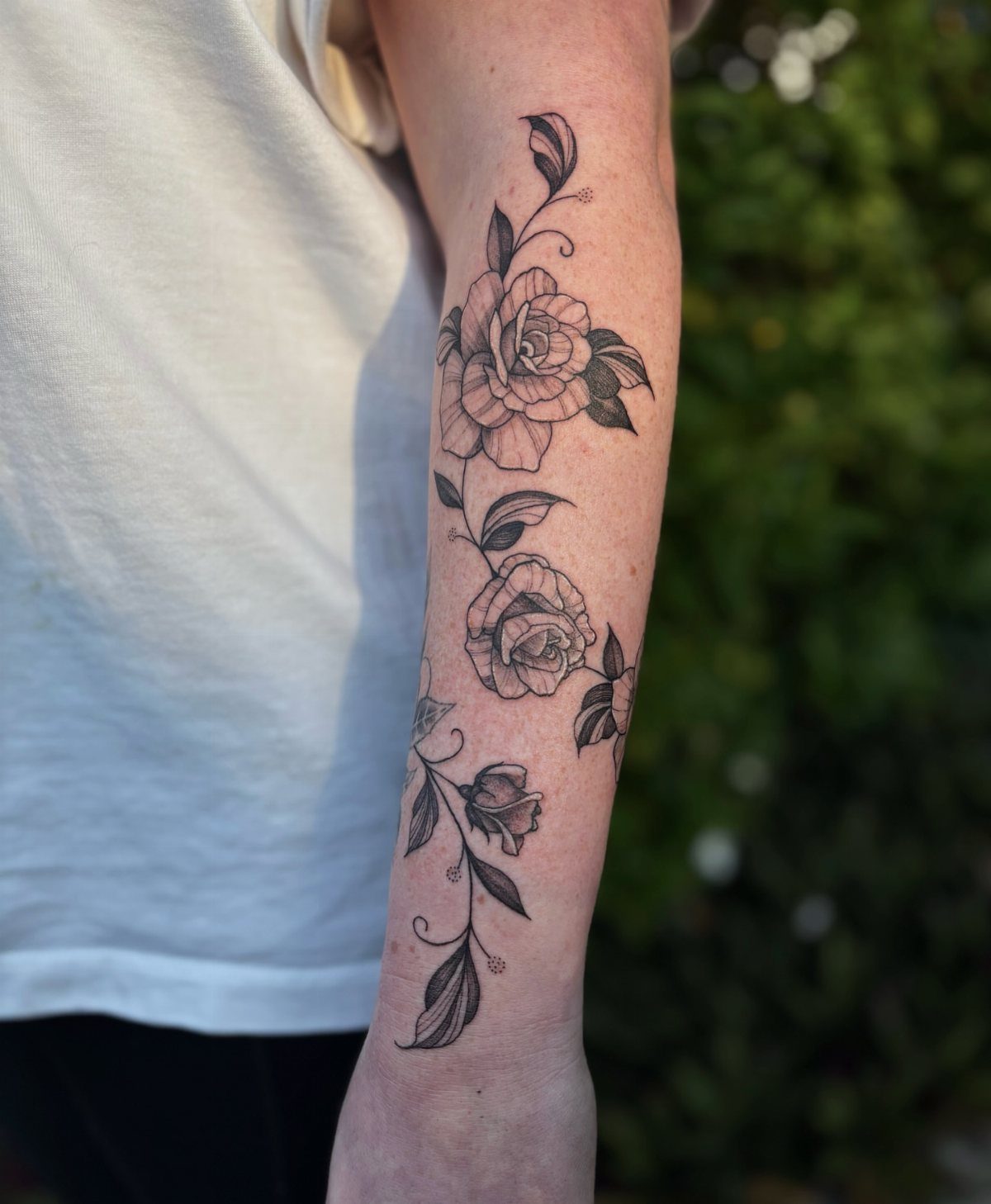 A black ink floral tattoo with roses and leaves on a person's forearm.