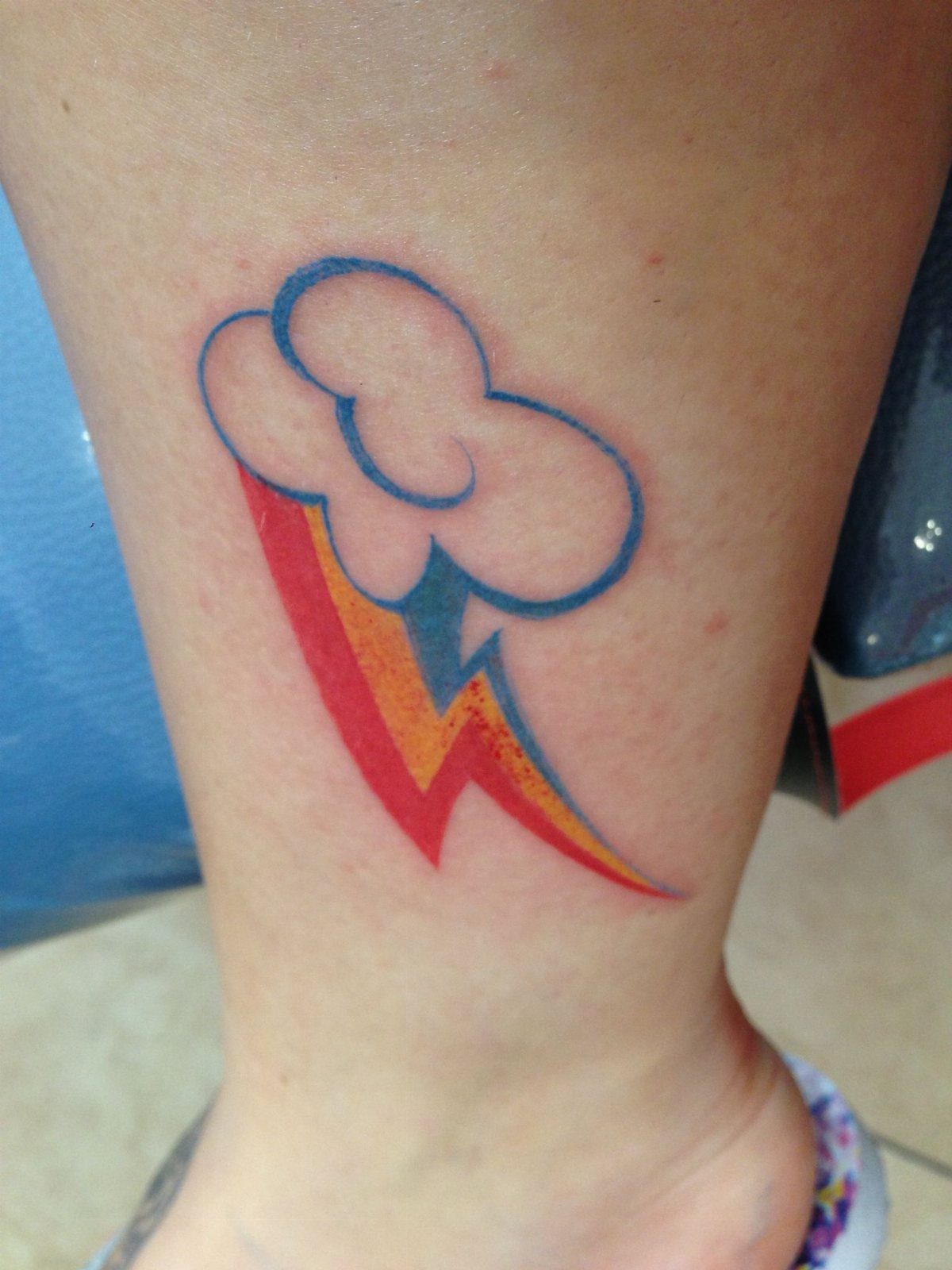 A colorful tattoo of a white cloud and a red and yellow lightning bolt on a leg.