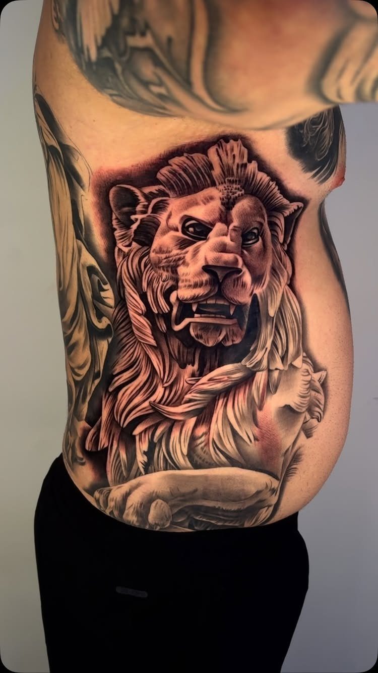 A large black and grey lion head tattoo covering a person's side and stomach area.