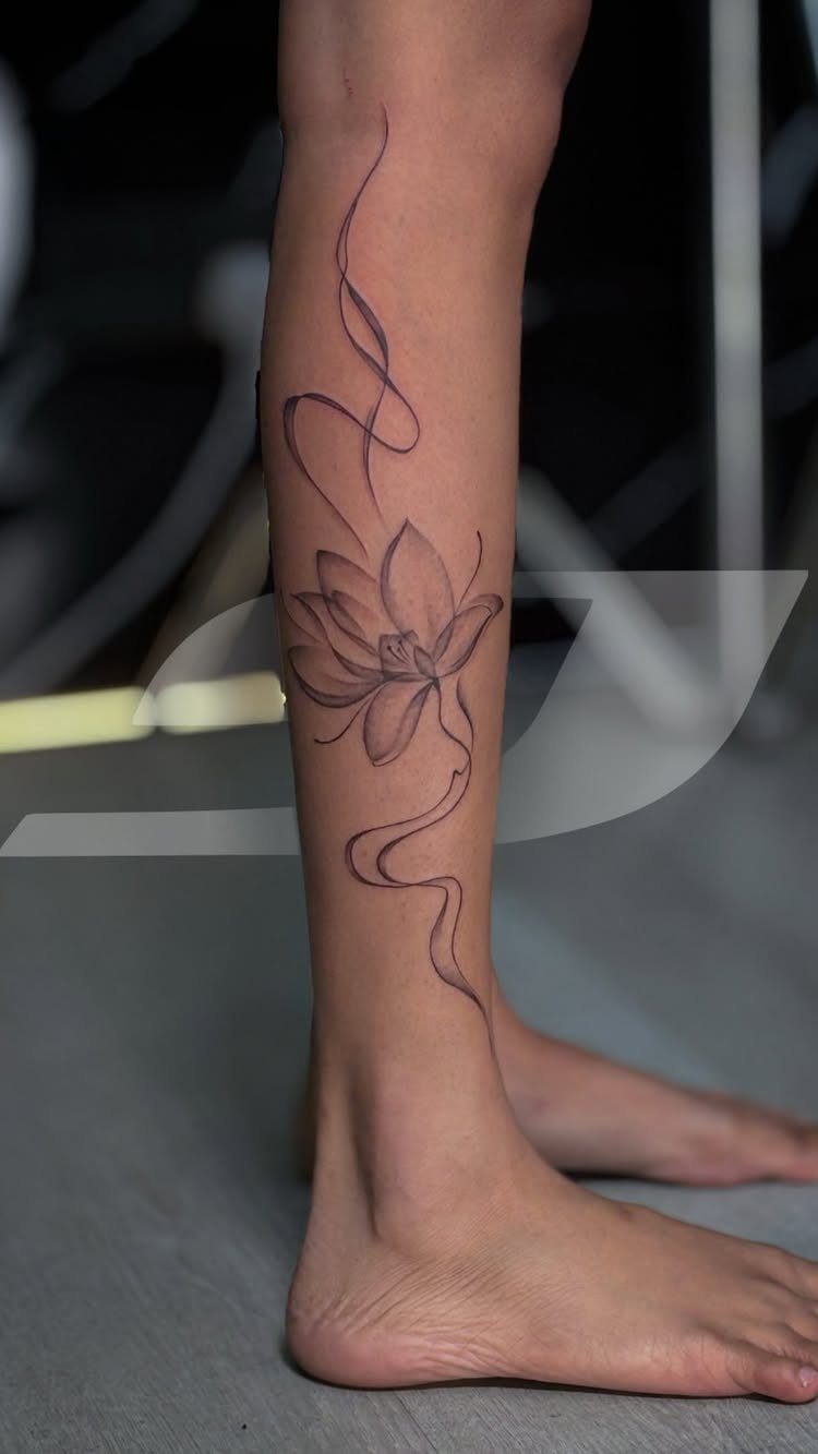 A fine line lotus flower tattoo with flowing wavy lines on a person's lower leg.