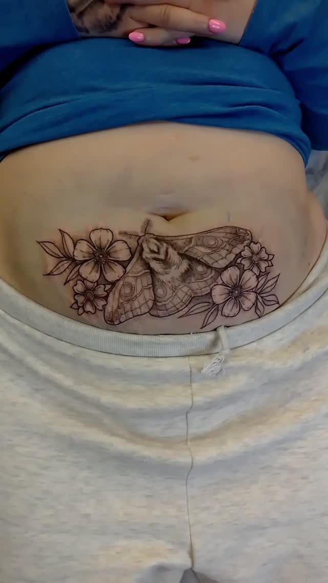 A moth and floral black ink tattoo centered on a person's stomach area.