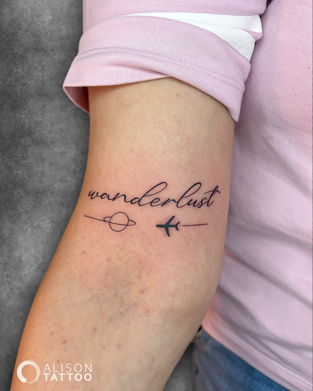 A minimalist wanderlust tattoo with a small planet and airplane on a person's arm.